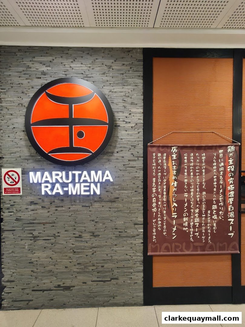 The exterior of Marutama Ramen, featuring its logo, name, and a banner with Japanese text.