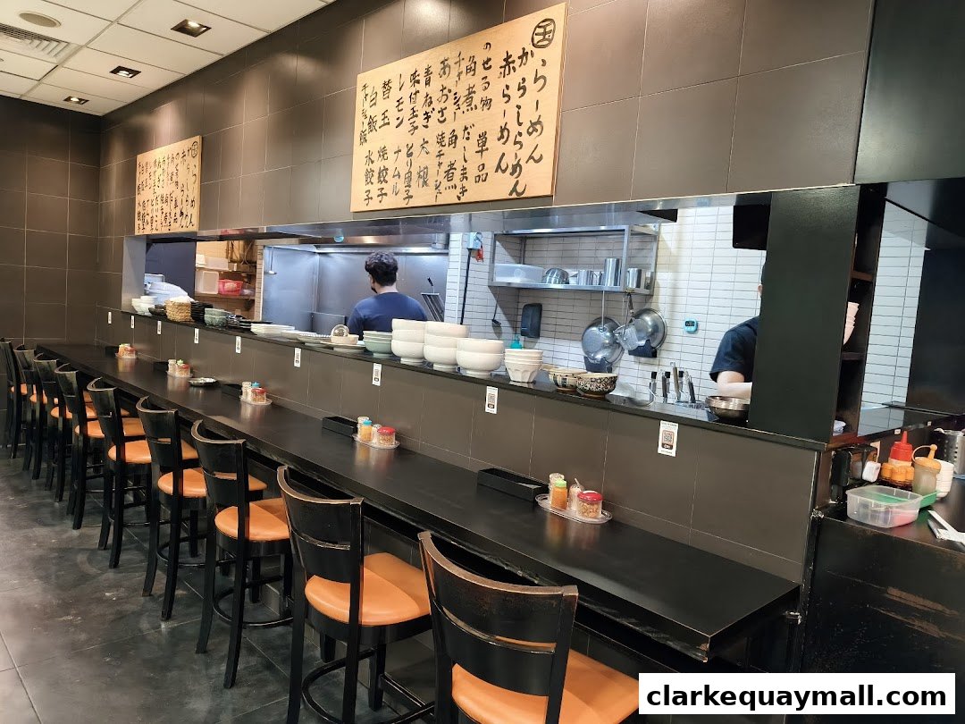Interior view of Marutama Ramen with a long counter, bar stools, and kitchen staff visible.