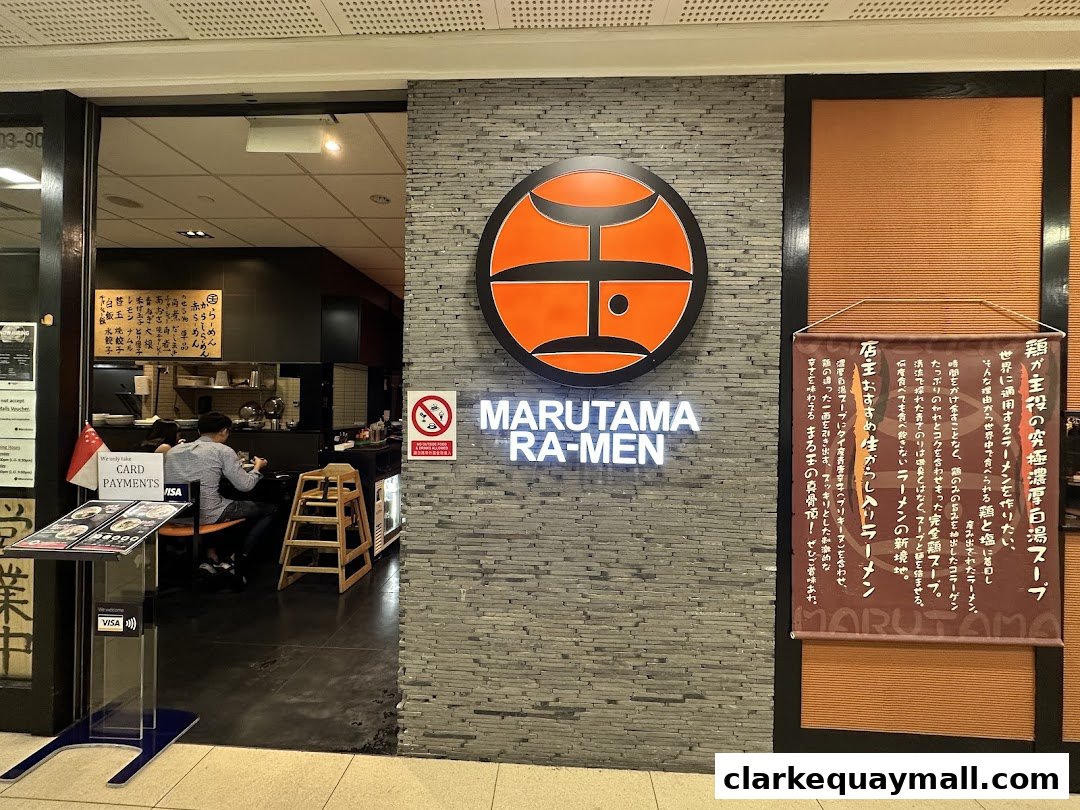 The entrance of Marutama Ramen, featuring its logo, signage, and a banner with Japanese text.