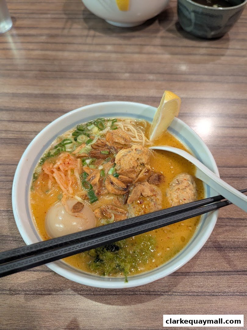 A steaming bowl of ramen with meatballs, egg, and a lemon slice, ready to be enjoyed.