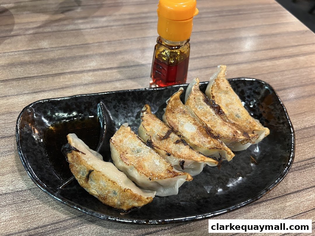 A plate of golden-brown pan-fried gyoza dumplings with dipping sauce and a small bottle of chili oil.
