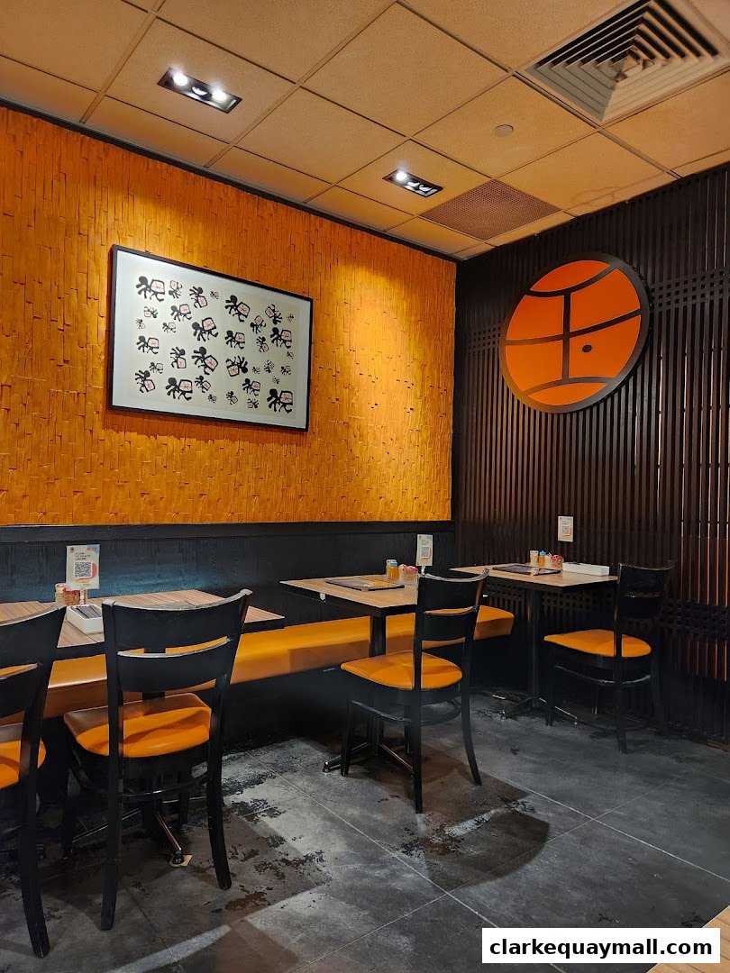 Interior of Marutama Ramen with orange seating, tables, and artwork on the wall.