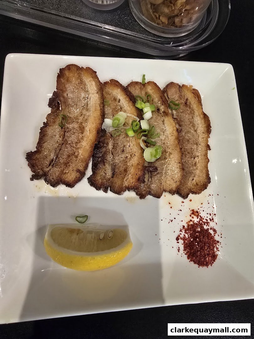 A plate of sliced chashu pork with green onions, lemon, and chili flakes.