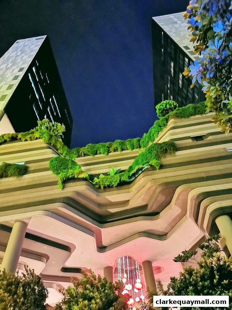 Modern architecture with layered balconies, lush greenery, and illuminated decorations at night.
