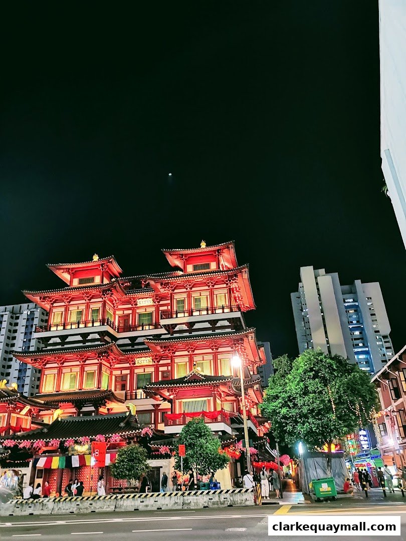 A vibrant night view of a traditional red and gold temple building with people walking nearby.