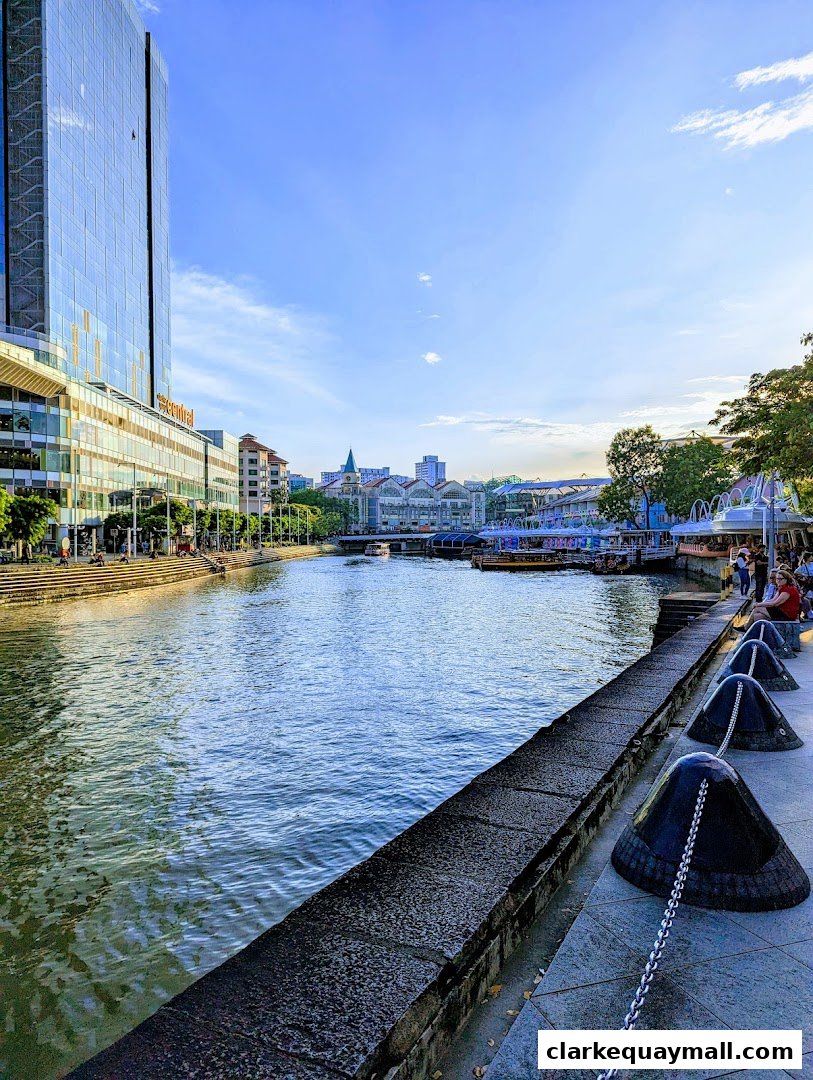 A scenic view of a river with buildings and people along the banks under a blue sky.