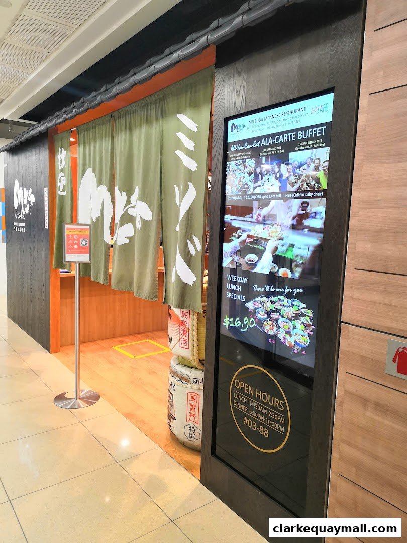 The entrance of Mitsuba Japanese Restaurant with a digital menu display and traditional green curtains.