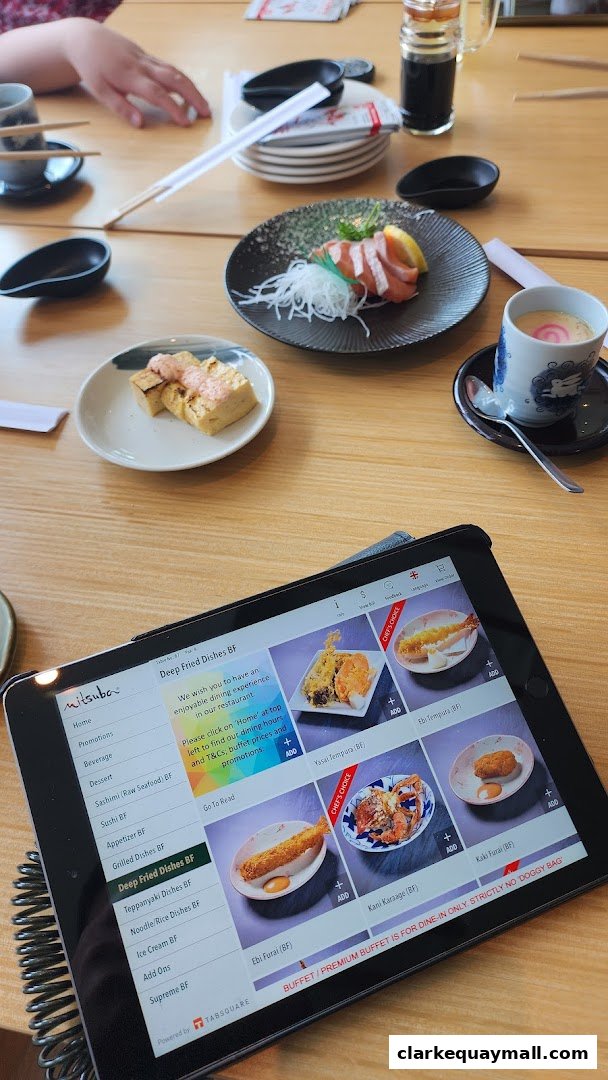 A tablet displays a digital menu for Mitsuba Japanese Restaurant with various dishes.