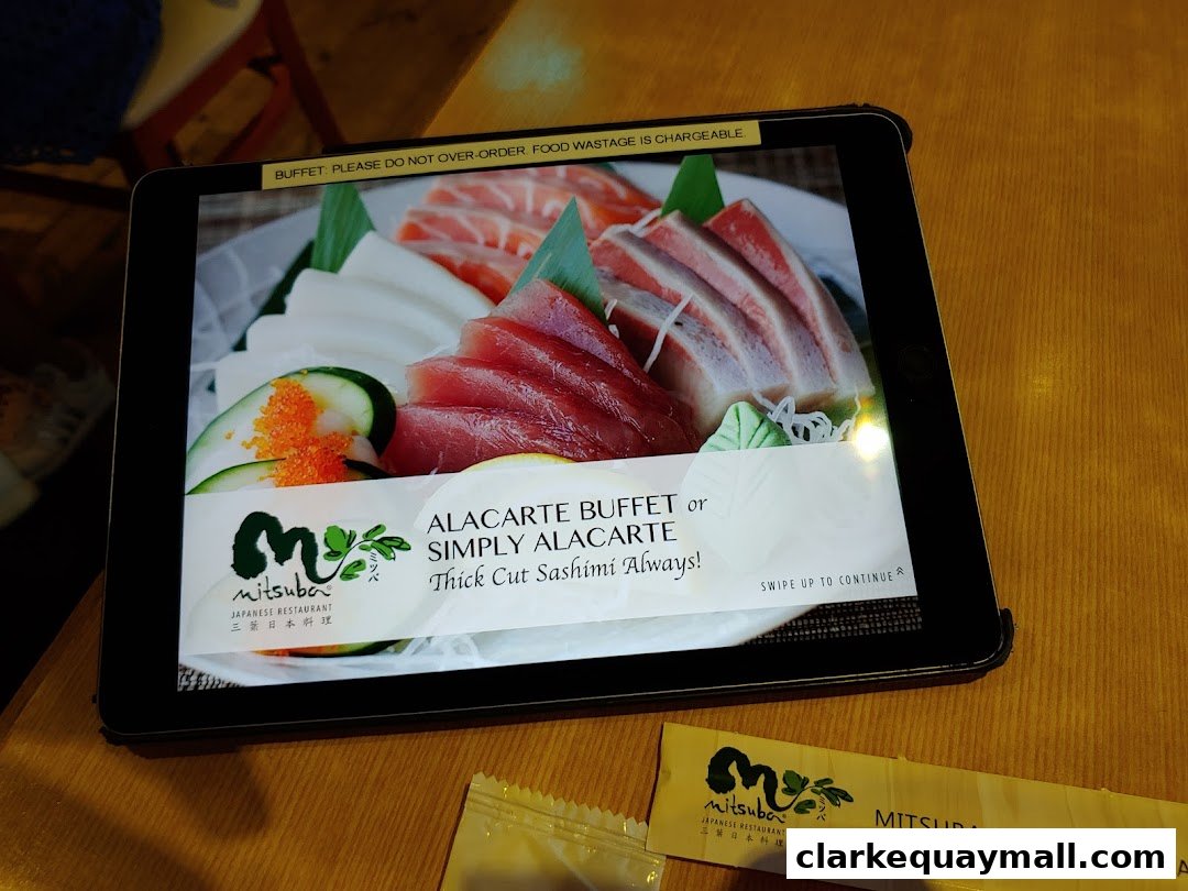 A tablet displays a vibrant image of sashimi with the Mitsuba Japanese Restaurant logo.