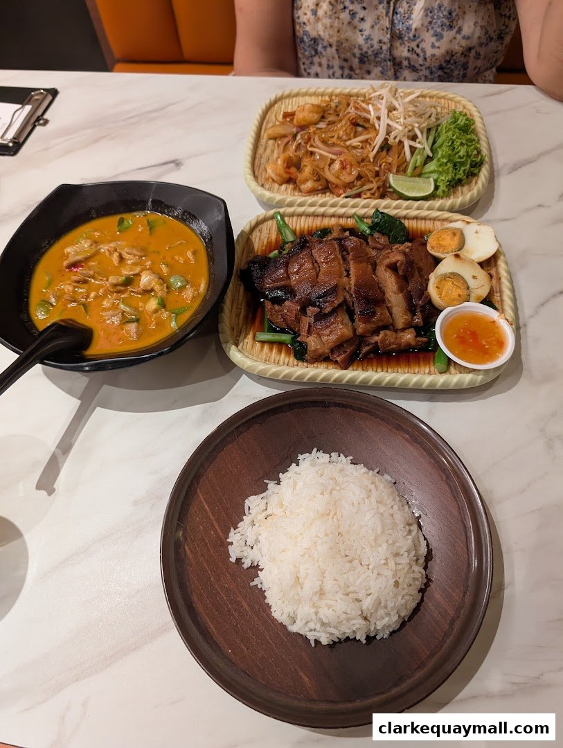 A table laden with delicious Thai dishes including Pad Thai, curry, roasted meat, and rice.