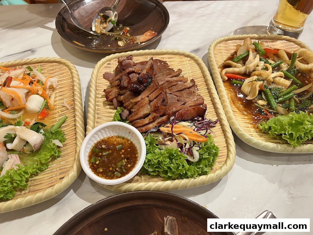 Three plates of Thai food, including grilled meat and seafood salads, are served on a table.