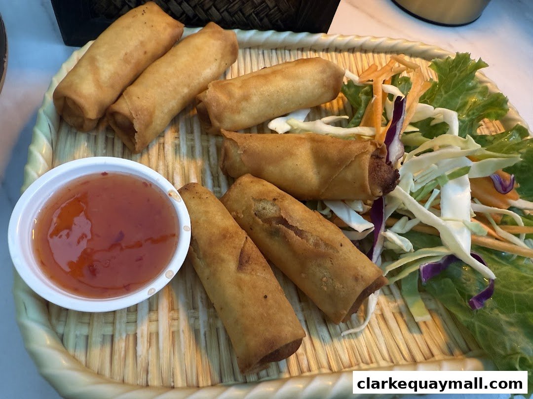 A platter of golden-brown spring rolls served with a side of sweet chili sauce and fresh salad.