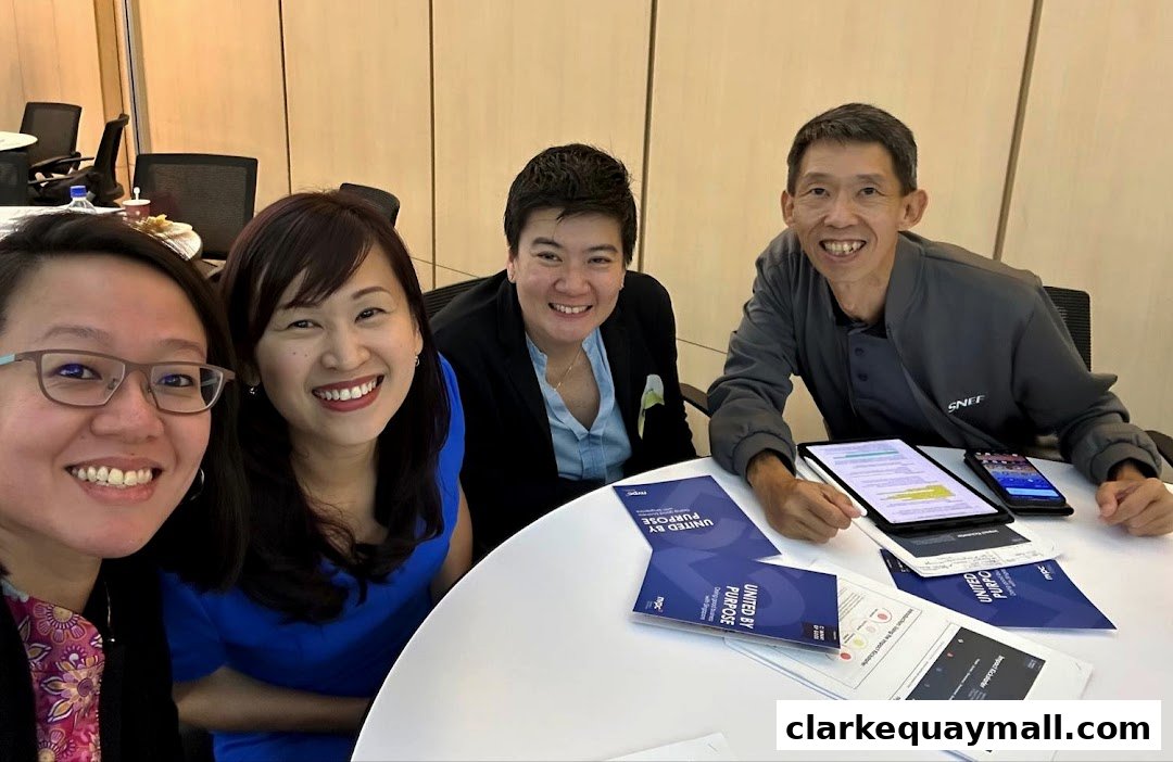 Four smiling individuals are gathered around a table, looking at documents and devices.