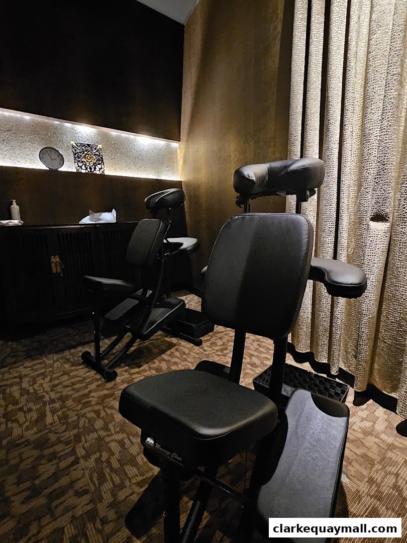 Two black massage chairs are set up in a dimly lit room with patterned curtains and decorative shelves.