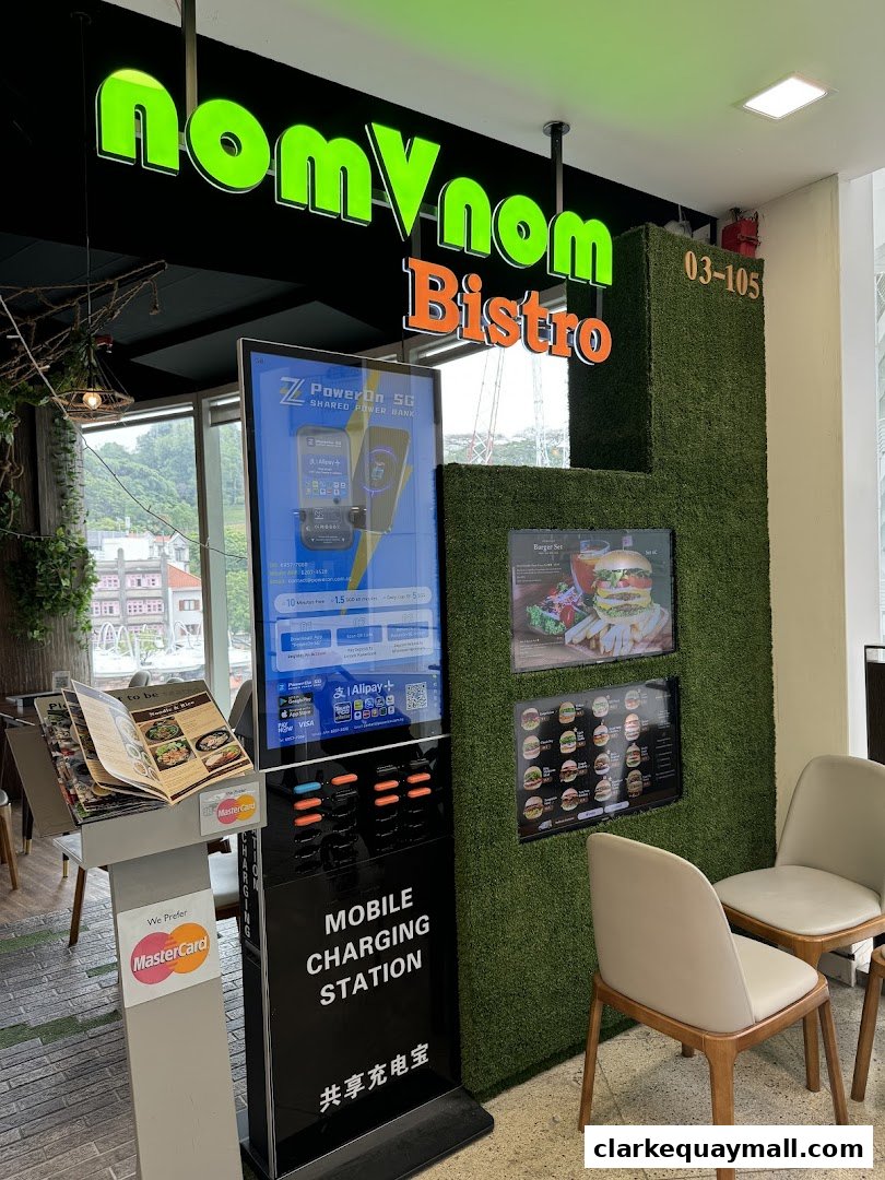 The entrance of nomVnom Bistro features a prominent sign, a mobile charging station, and seating.