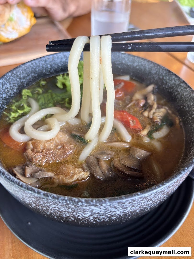 A close-up shot of a steaming bowl of udon noodles with vegetables and mushrooms.