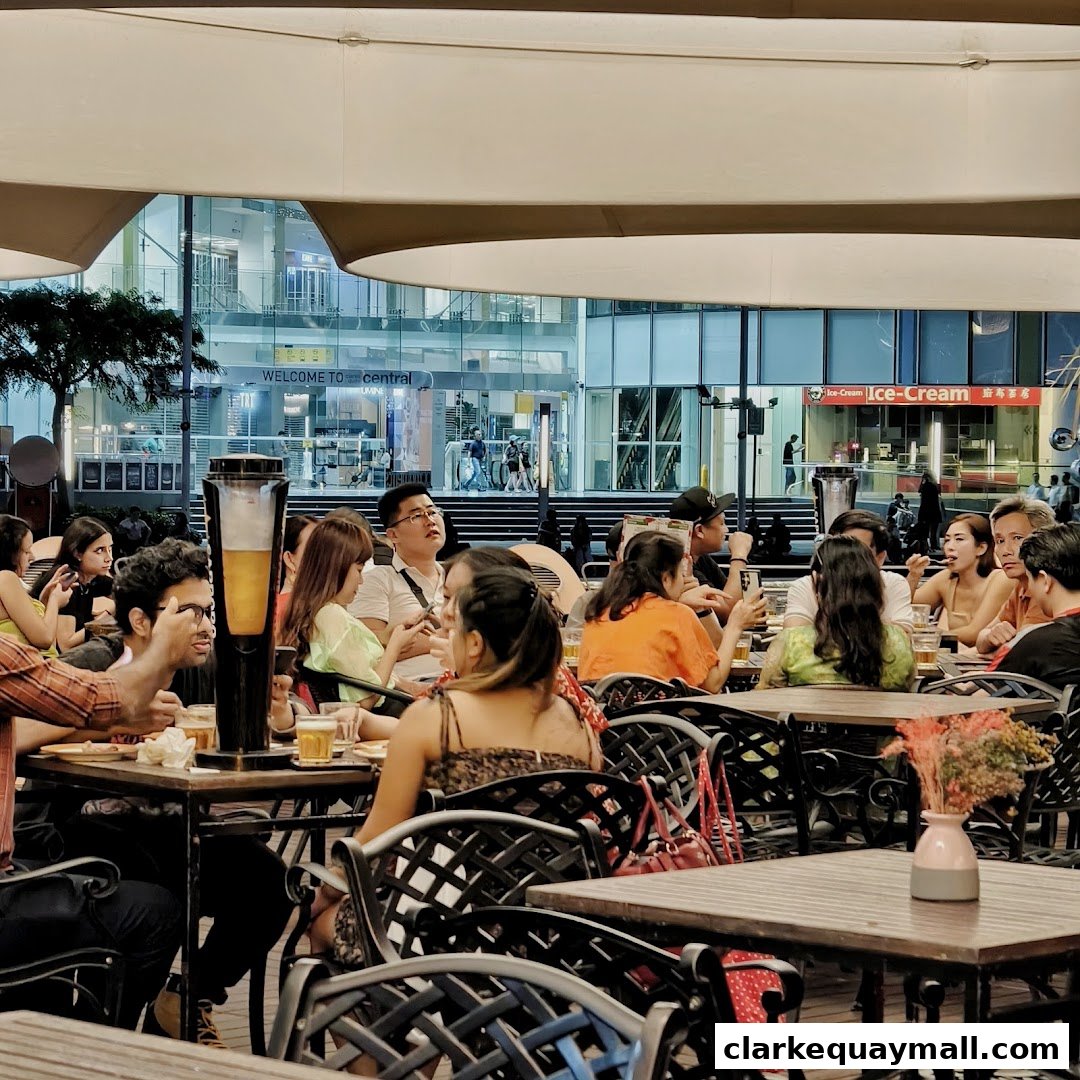 People dining and drinking at tables outside a restaurant with a modern building in the background.