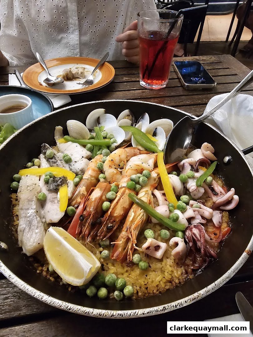 A large pan of seafood paella with prawns, squid, fish, peas, and lemon.