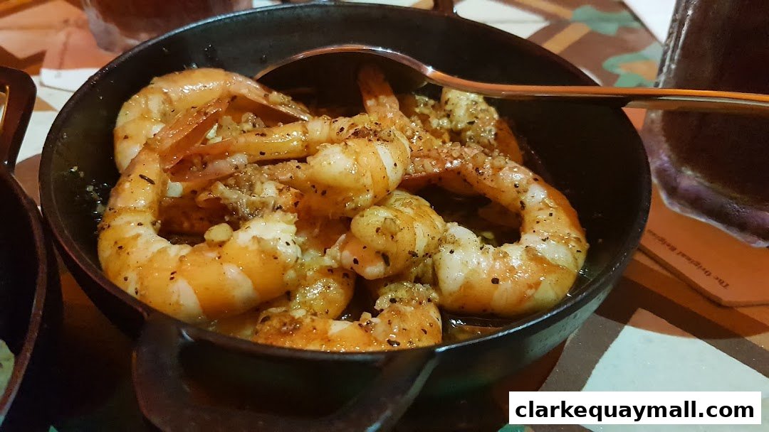 A close-up shot of a sizzling garlic shrimp tapa served in a black cast iron dish.