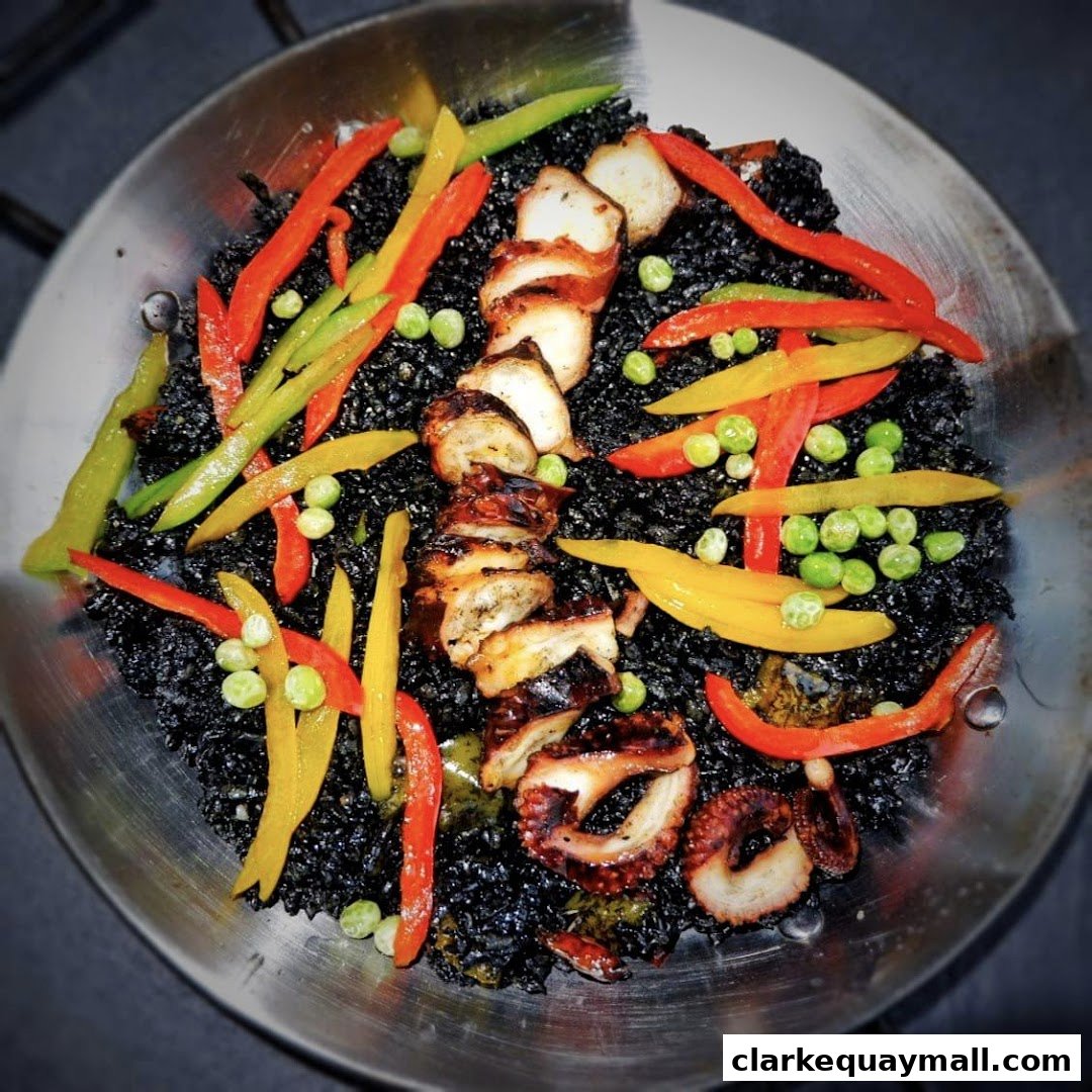 A close-up of a black rice dish with grilled octopus and colorful bell peppers.