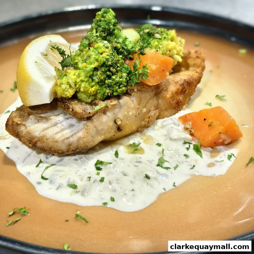 A close-up of a delicious fish dish with broccoli, carrots, lemon, and sauce.