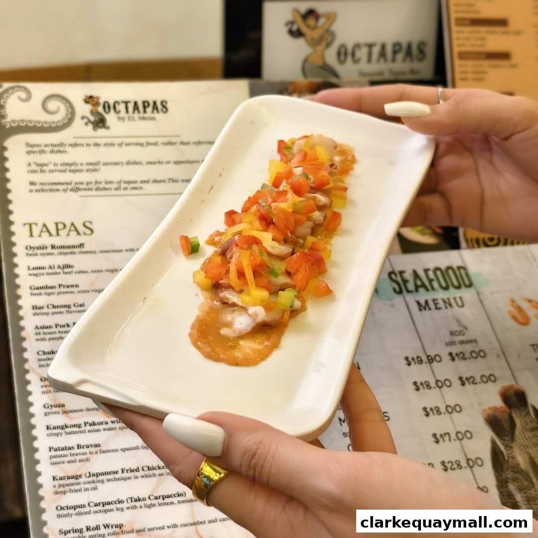 A person holds a plate of tapas with a menu from Octapas restaurant in the background.