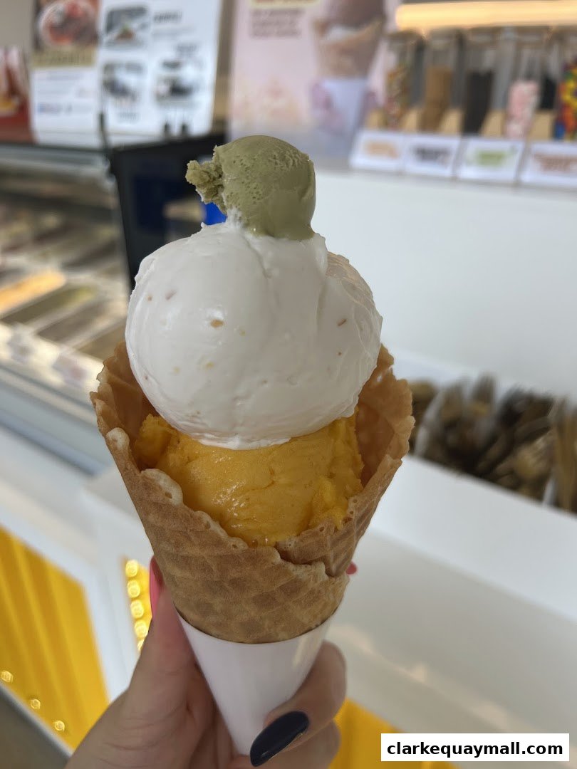 A hand holds a waffle cone with three scoops of ice cream, including mango and matcha flavors.