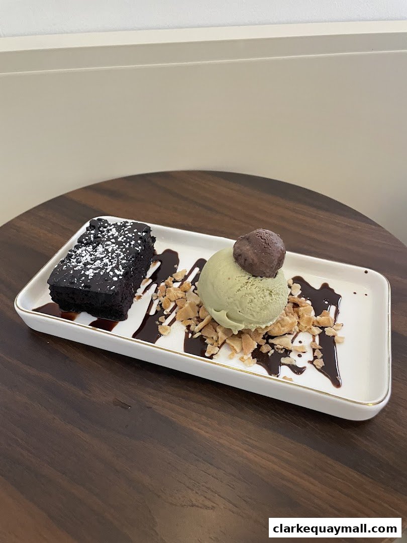 A chocolate brownie with green tea ice cream and chocolate sauce on a white plate.