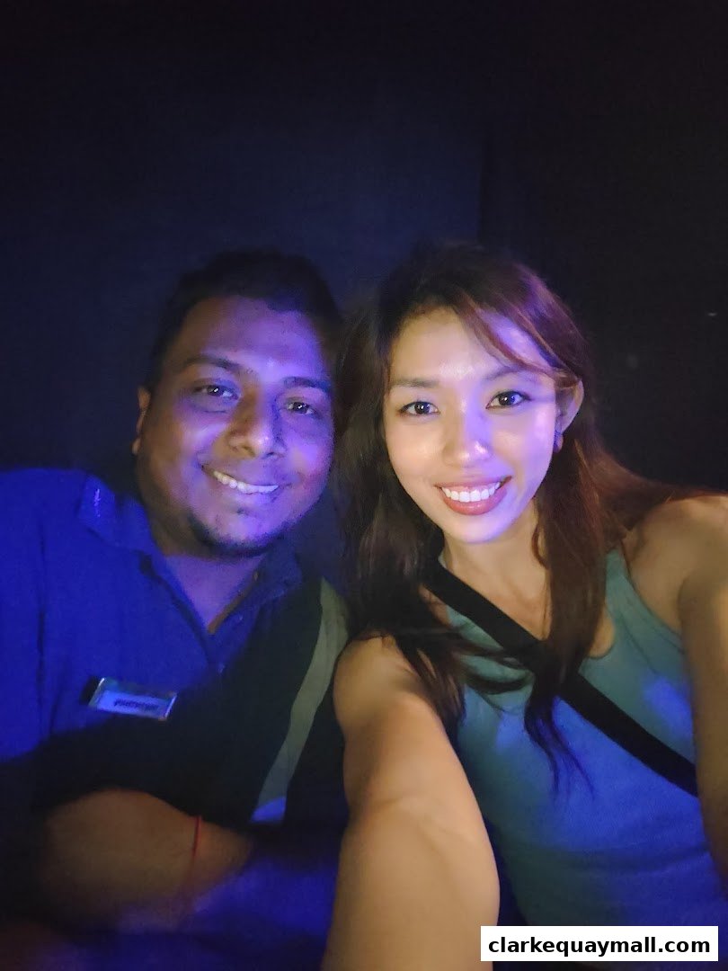 A man and a woman smiling at the camera in a dimly lit environment.