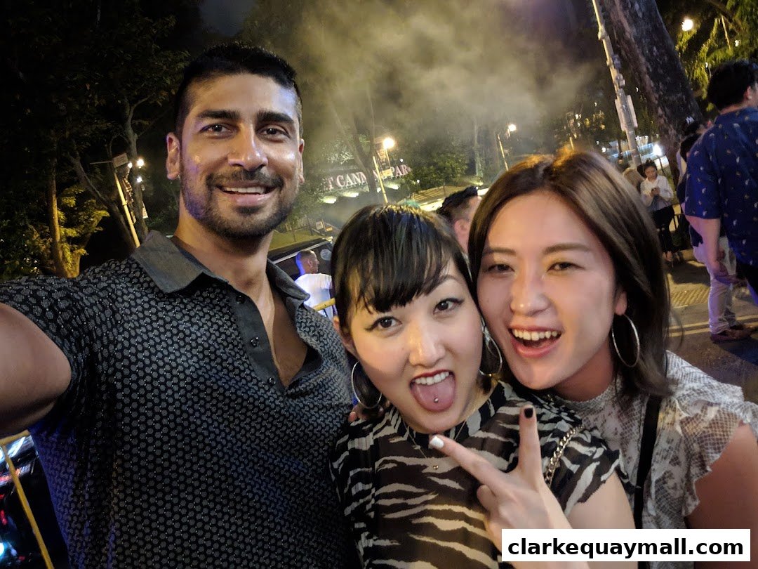 Three friends smiling and posing for a photo at an outdoor event at night.