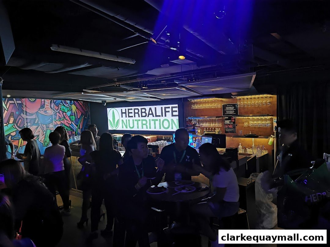 People gathered inside a dimly lit venue with a prominent HerbaLife Nutrition logo.