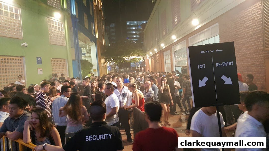 A large crowd of people gathered outside a venue at night, with a sign indicating exit and re-entry.