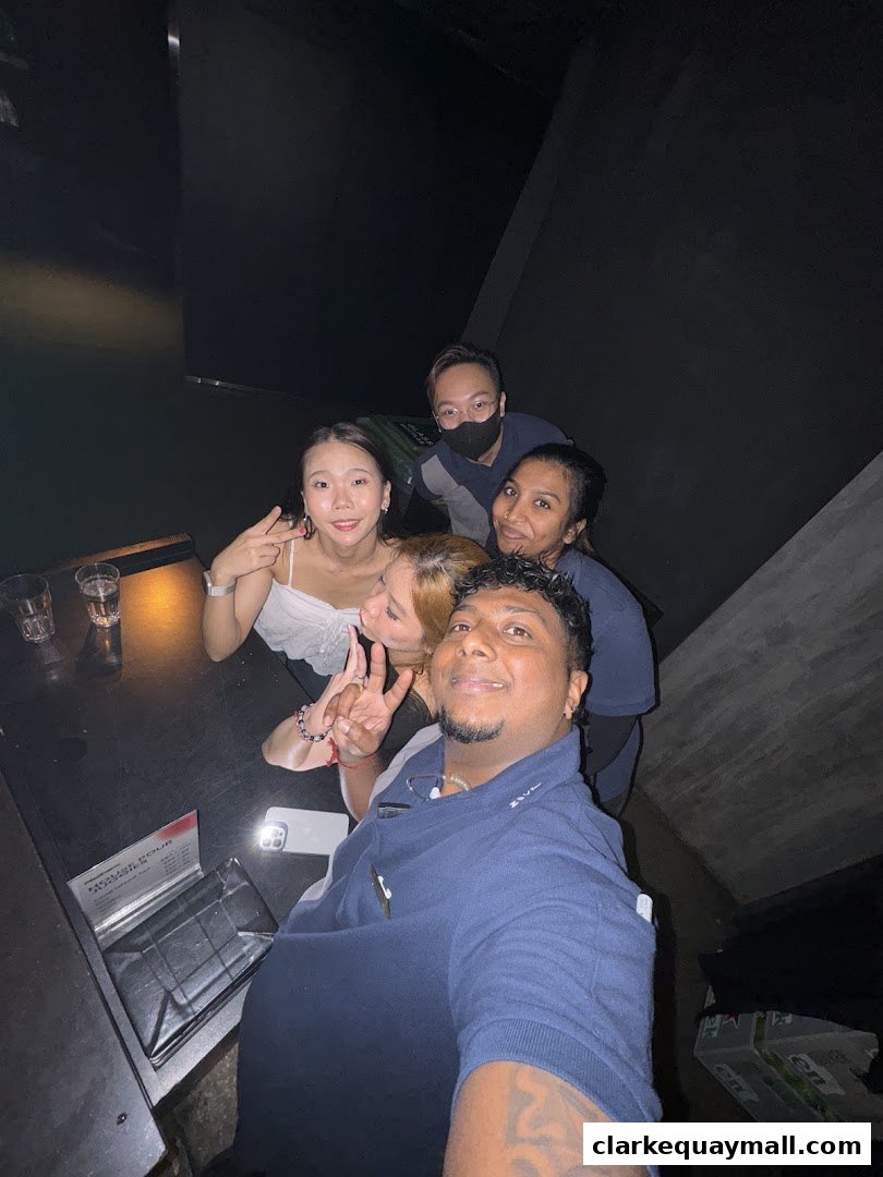 A group of friends posing for a selfie at a table in a dimly lit venue.