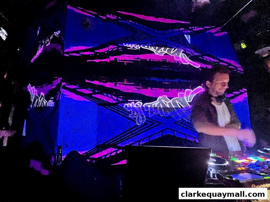 A DJ plays music in front of a vibrant, illuminated stage with abstract graphics.