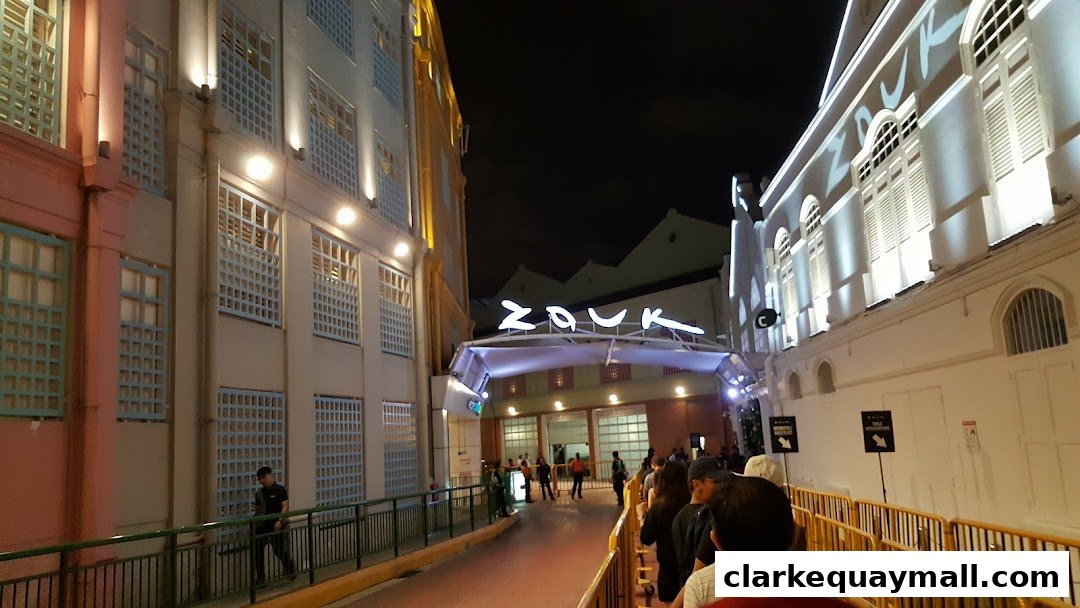 People queuing outside a brightly lit building with a prominent "Zouk" sign at night.