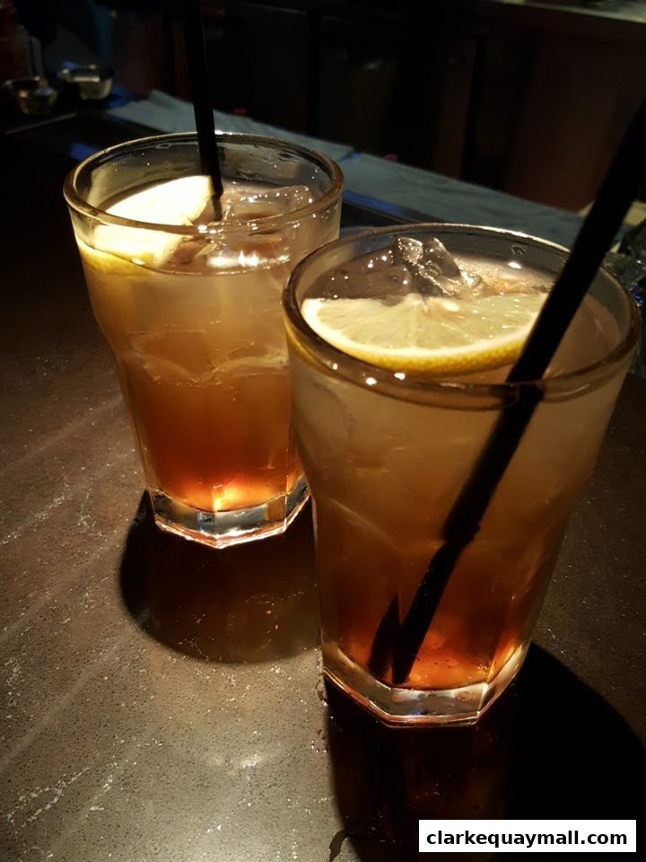 Two refreshing iced drinks with lemon slices and straws on a dark countertop.