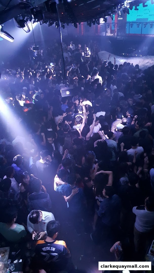 A crowded nightclub with people dancing under dramatic lighting and spotlights.