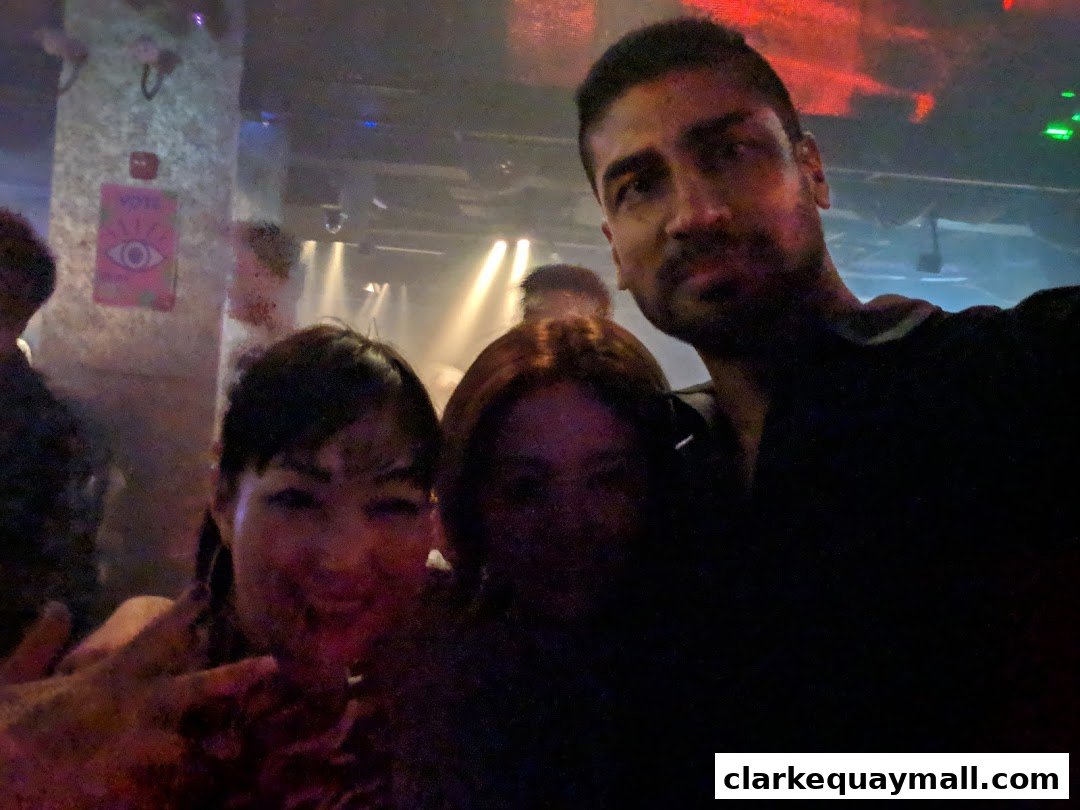 Three friends posing for a selfie in a dimly lit venue with colorful lights.