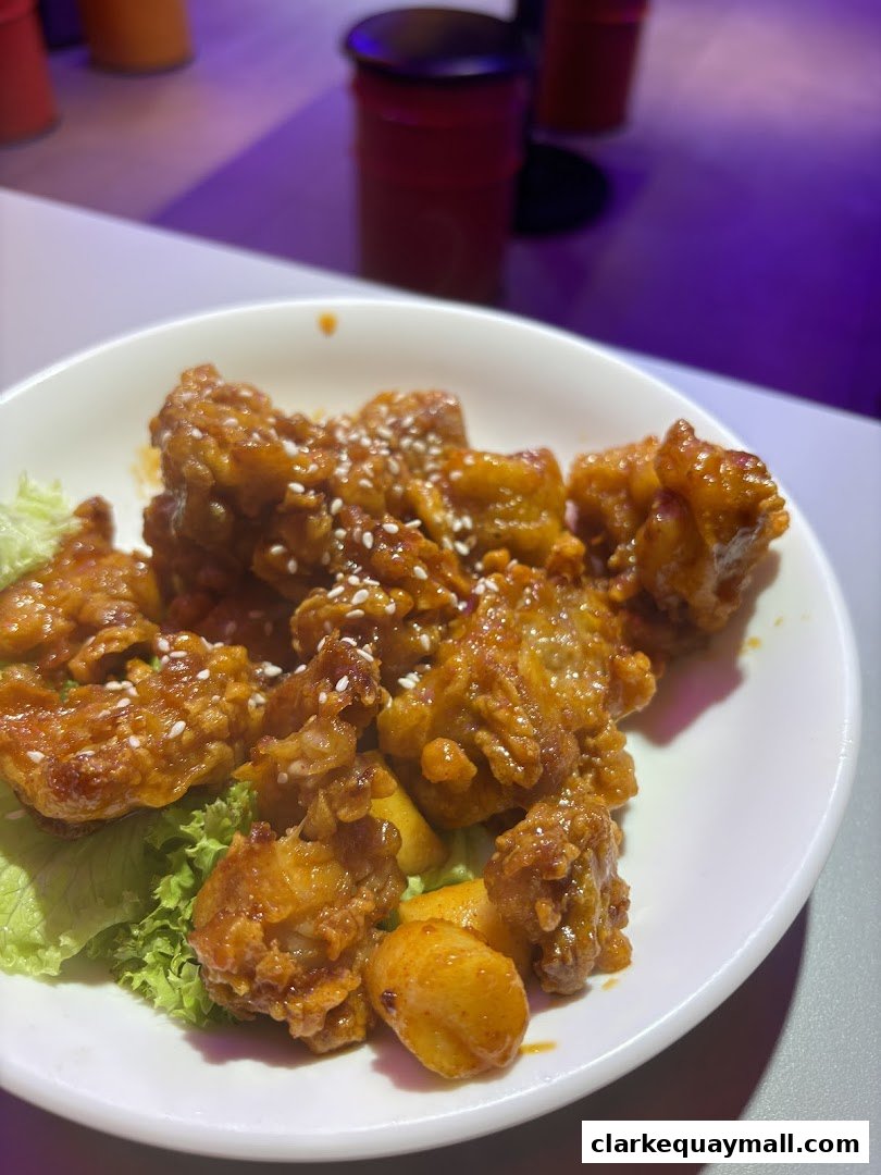 A close-up of Korean fried chicken with tteokbokki and lettuce on a white plate.
