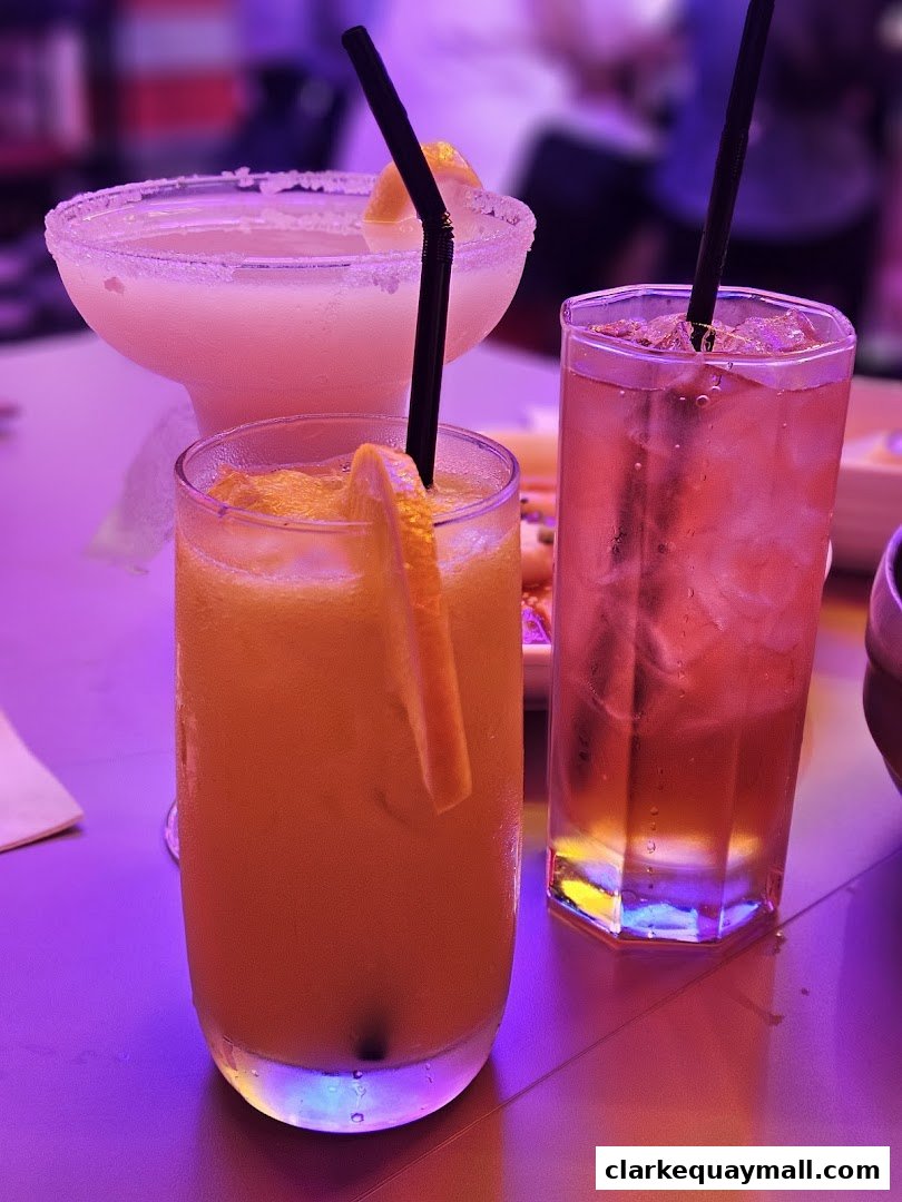 Three colorful cocktails with garnishes and straws, illuminated by purple lighting.