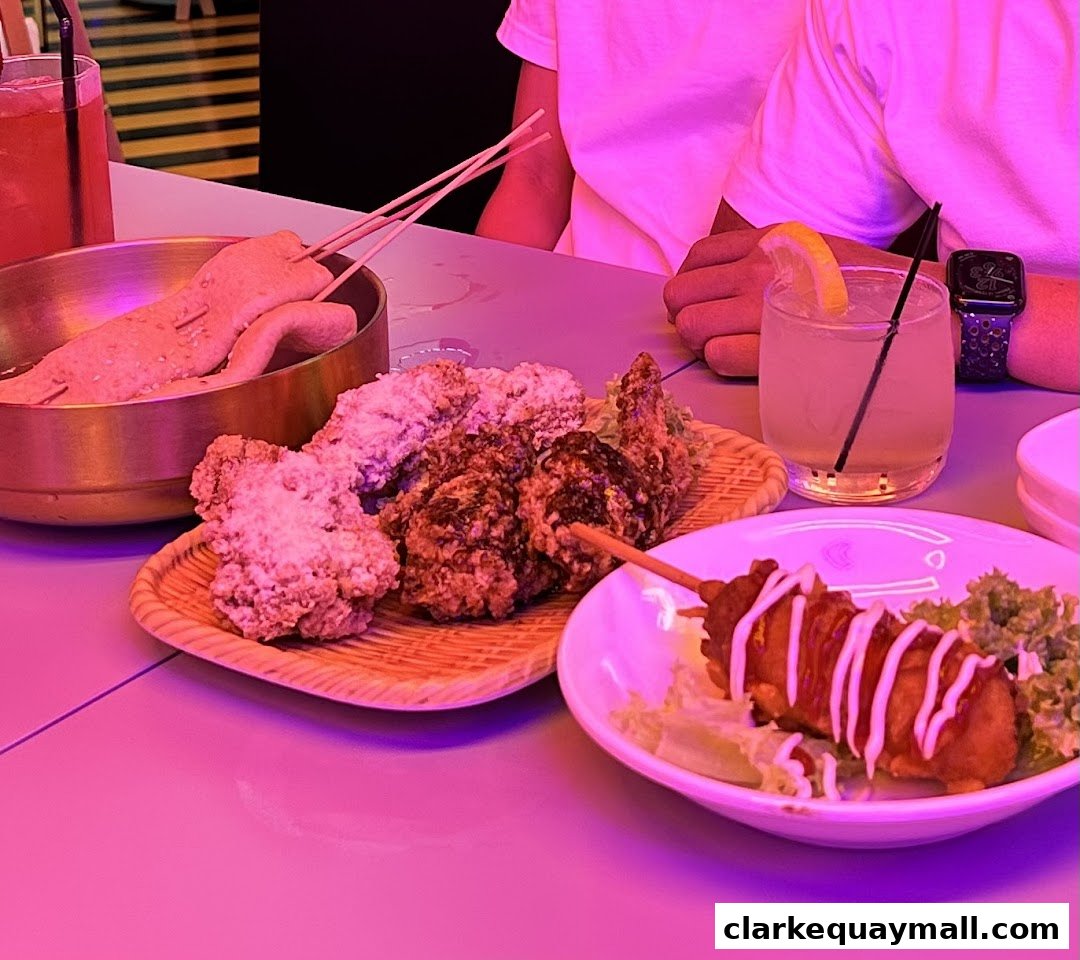A table laden with Korean street food, including fried chicken, fish cakes, and a corn dog, with drinks.