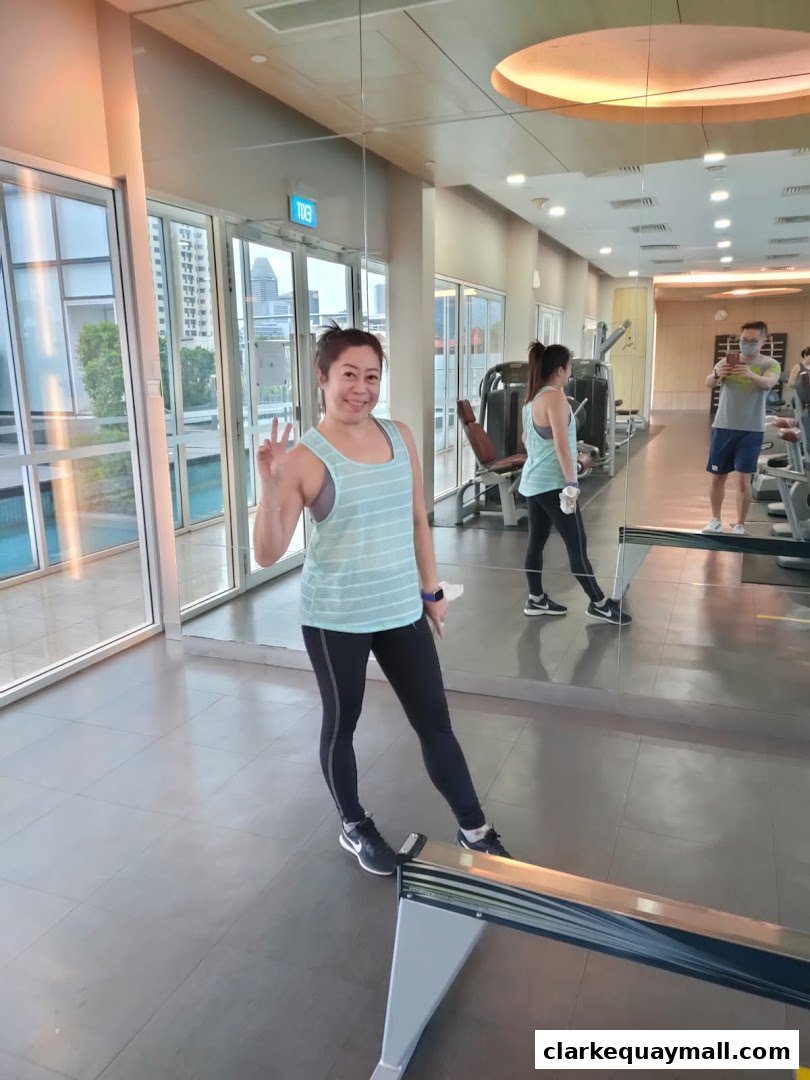 A woman in workout clothes poses with a peace sign in a gym with mirrors and exercise equipment.