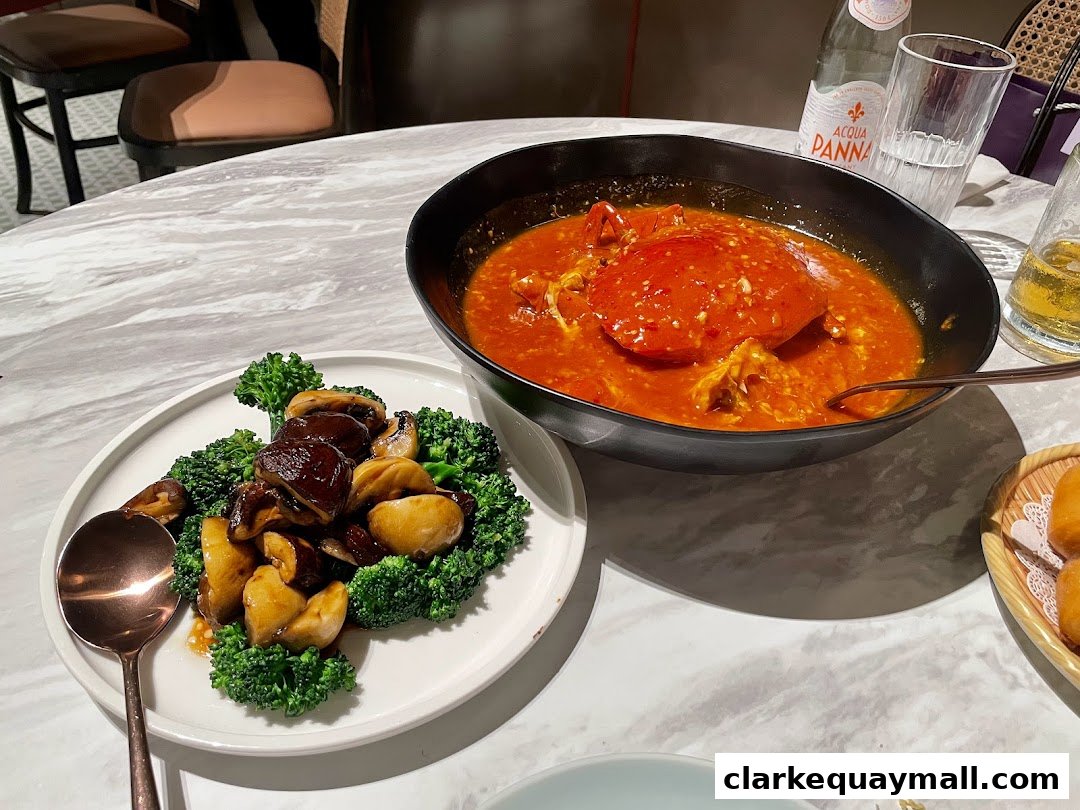 A table setting with a bowl of chili crab and a plate of broccoli and mushrooms.