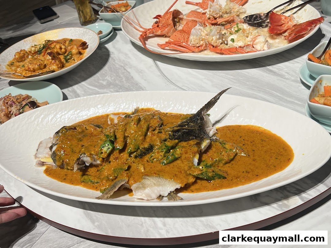 A table laden with delicious seafood dishes, including a whole fish in curry sauce and lobster.