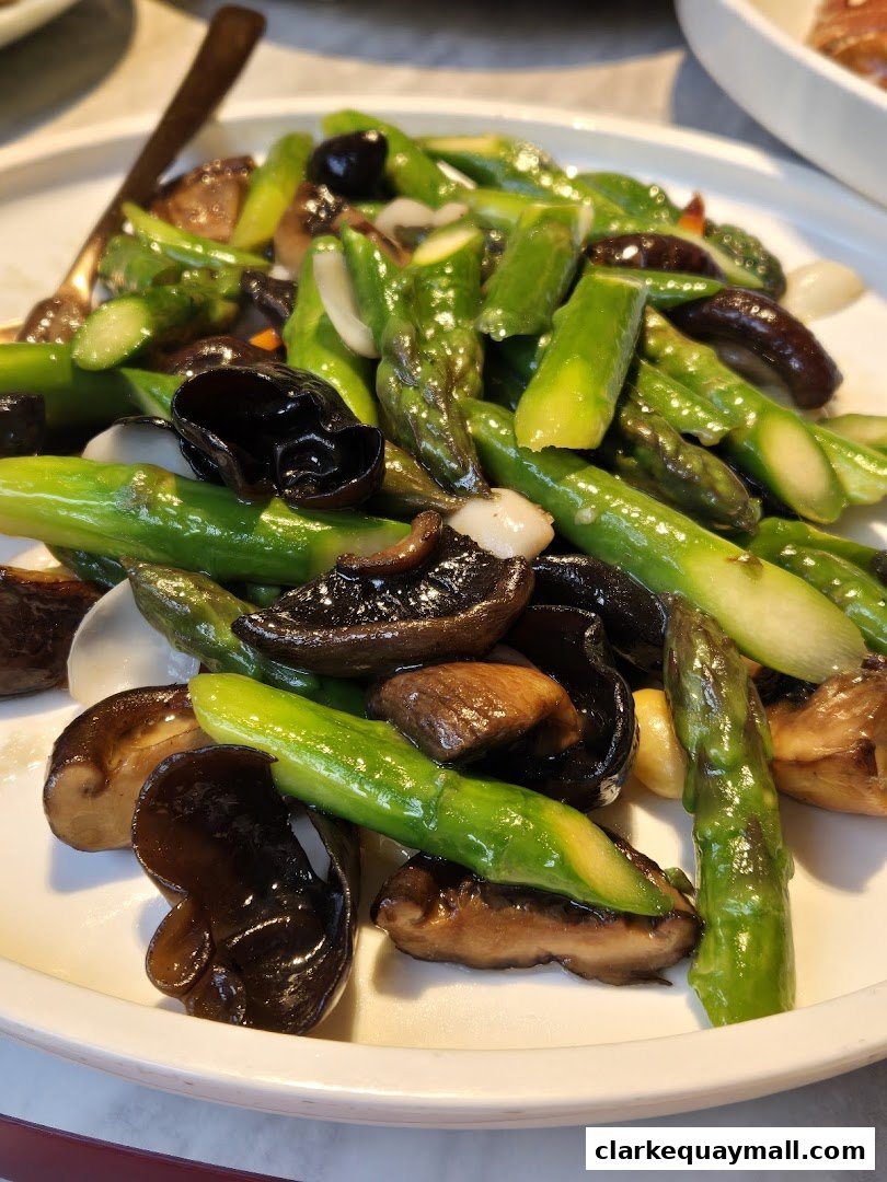 A plate of stir-fried asparagus with mushrooms and wood ear fungus.