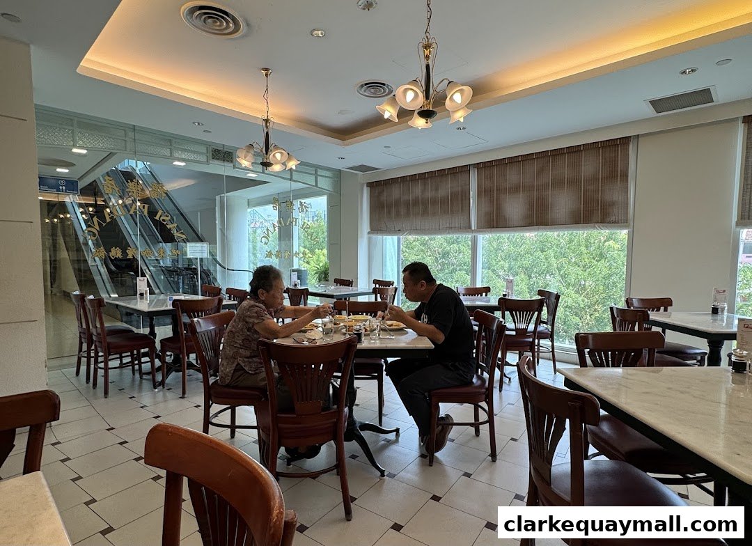 Diners enjoy a meal at Rendezvous Restaurant Hock Lock Kee, with an escalator visible through the glass.