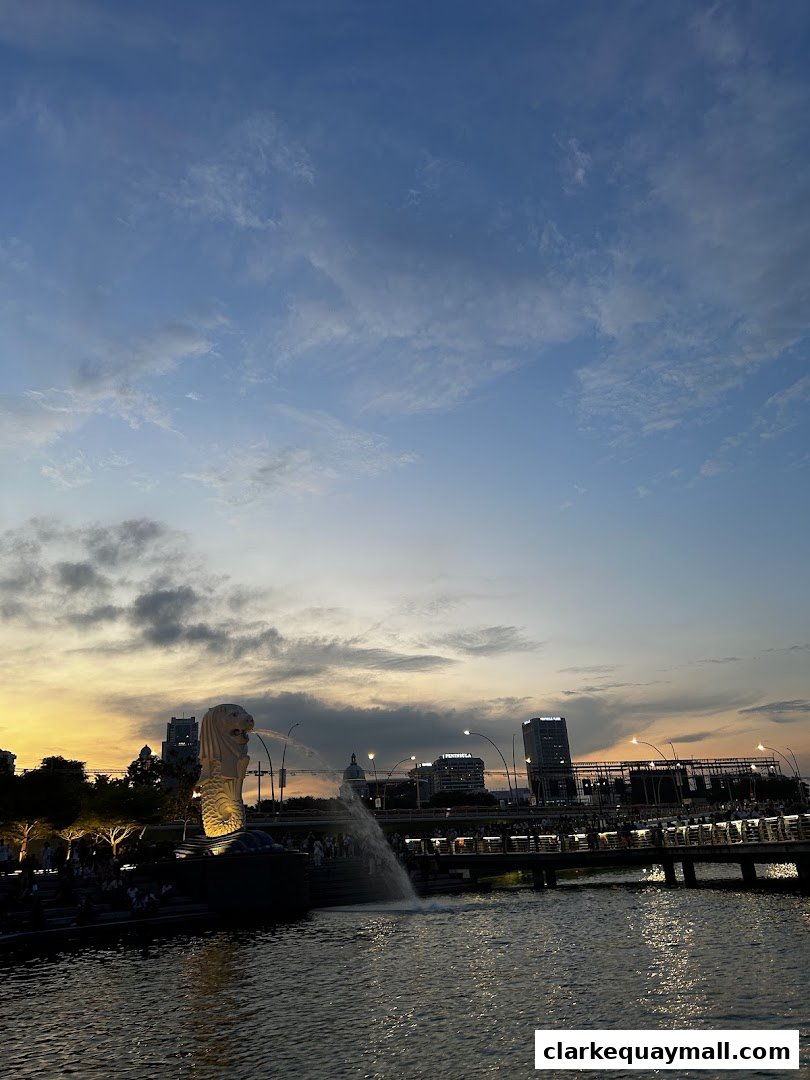 Merlion statue spouting water at sunset with city skyline and river.