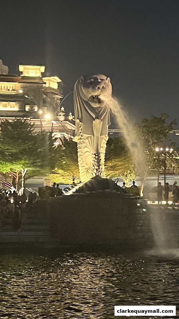 The iconic Merlion statue spouts water at night, with a crowd gathered around.