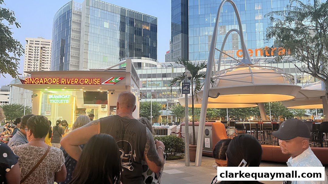 People queuing at a Singapore River Cruise ticket counter with modern buildings in the background.