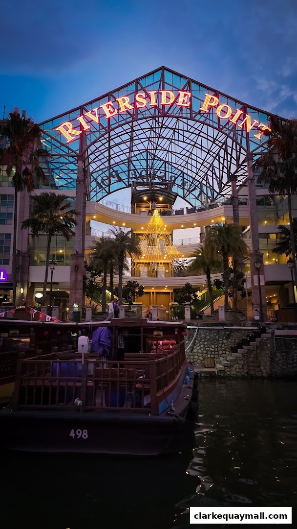 The illuminated 'RIVERSIDE POINT' sign above a multi-level building with boats docked in the water.